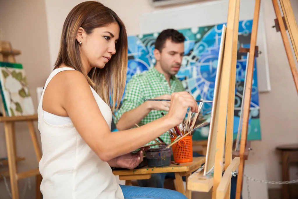Profile view of a couple of adults working on a painting at an art school
